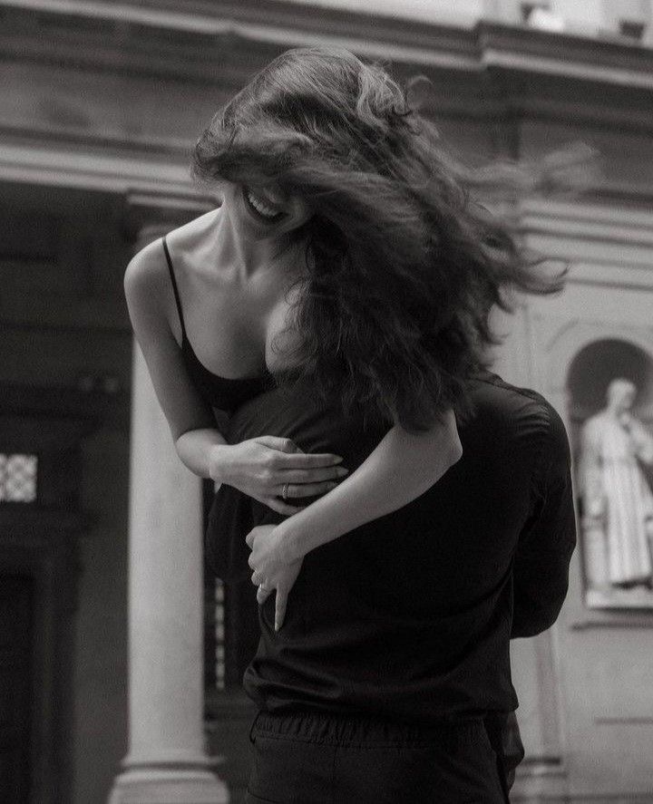 A couple embracing in the street, her face turned into his shoulder